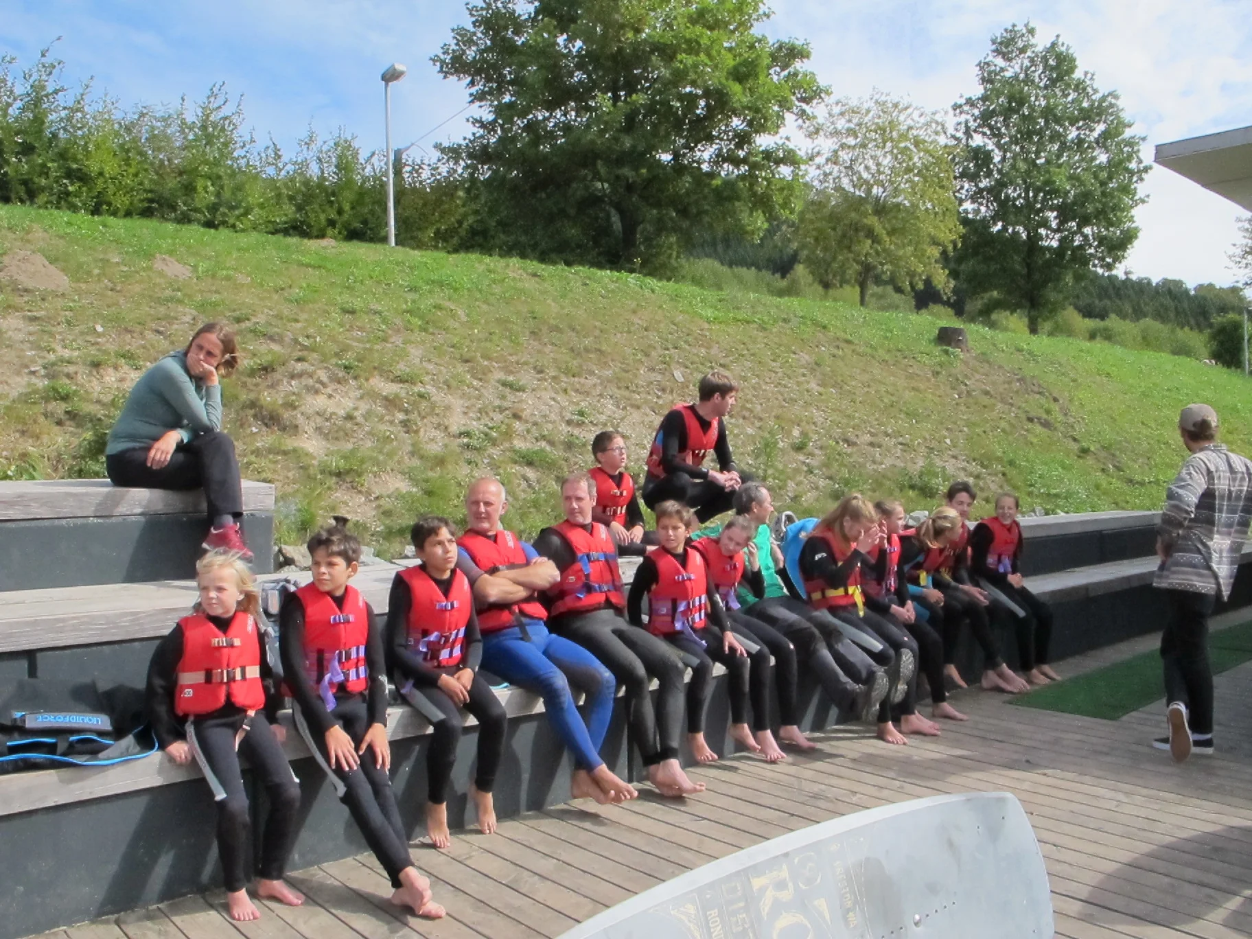 Jugendliche mit Neoprenanzügen und Schwimmwesten sitzen auf einer Holztribüne an einer Wassersportanlage. | © DAV Dortmund