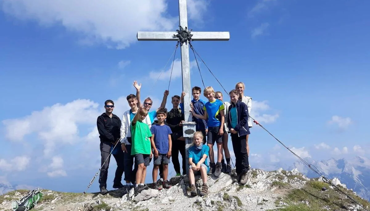 Eine Jugendgruppe steht bei Sonnenschein auf einem felsigen Gipfel vor einem großen Gipfelkreuz. | © DAV Dortmund