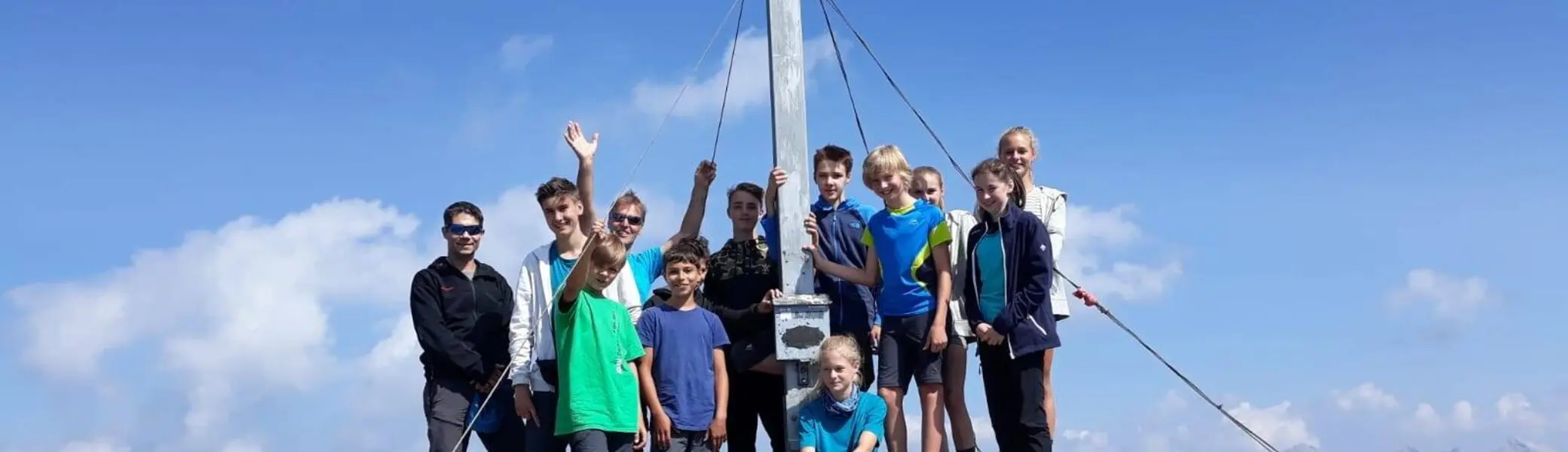 Eine Jugendgruppe steht bei Sonnenschein auf einem felsigen Gipfel vor einem großen Gipfelkreuz. | © DAV Dortmund