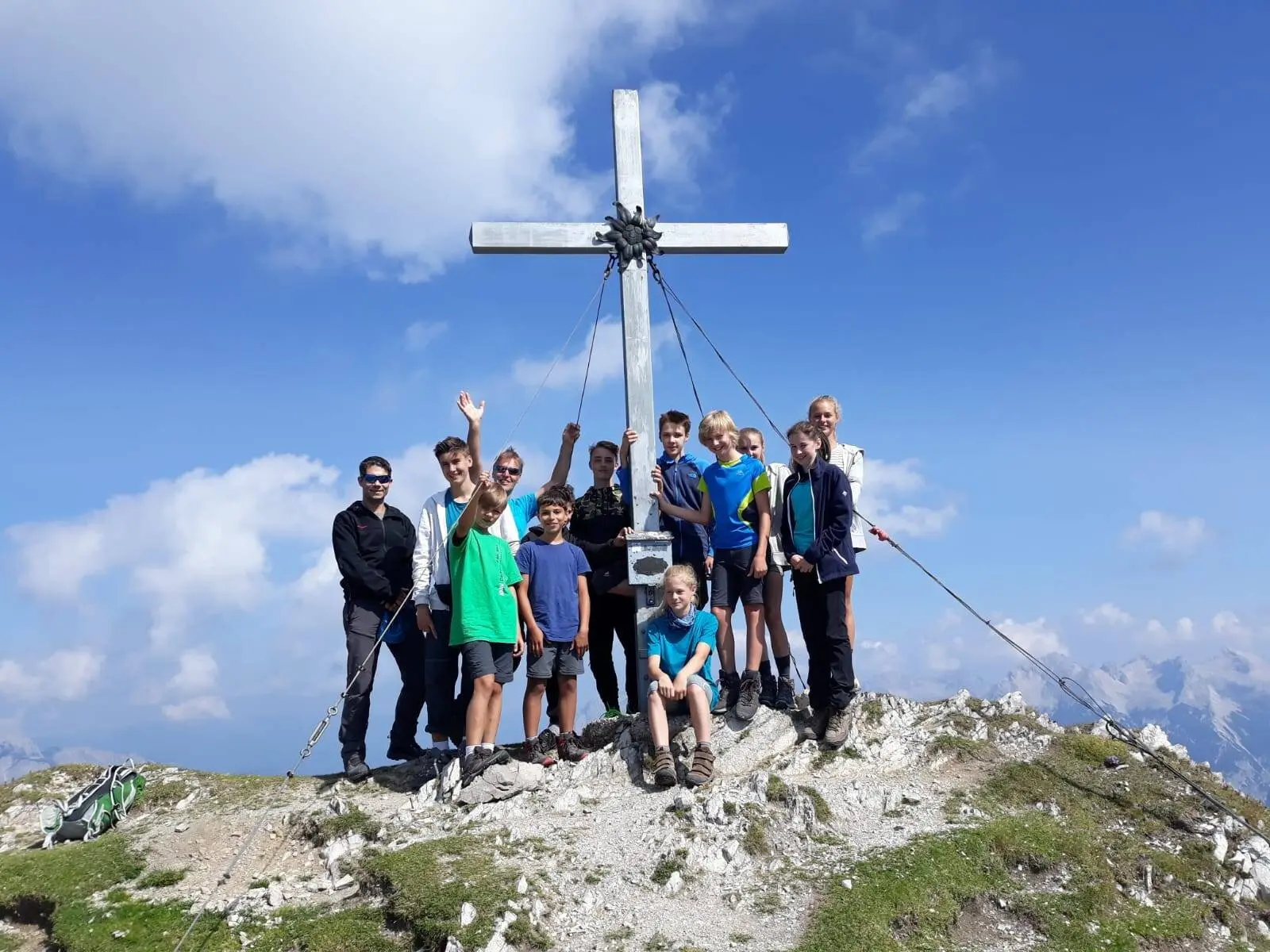 Eine Jugendgruppe steht bei Sonnenschein auf einem felsigen Gipfel vor einem großen Gipfelkreuz. | © DAV Dortmund