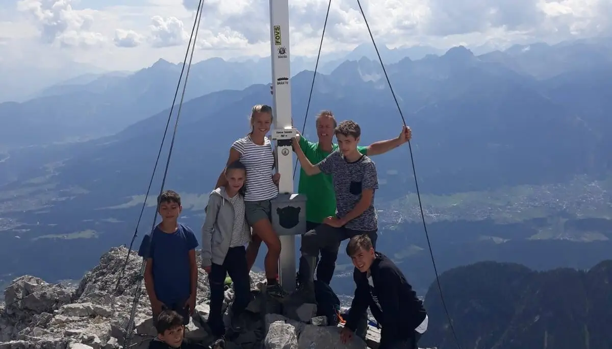Mehrere Jugendliche stehen unter einem weißen Gipfelkreuz auf einem felsigen Berg mit weitem Talblick im Hintergrund. | © DAV Dortmund
