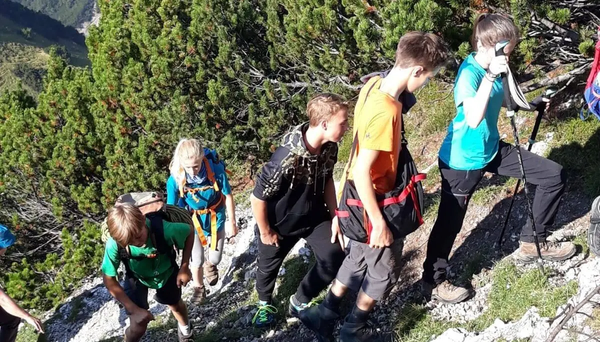 Eine Gruppe Jugendlicher wandert bergauf auf einem schmalen Pfad zwischen Nadelbäumen und Felsen. | © DAV Dortmund