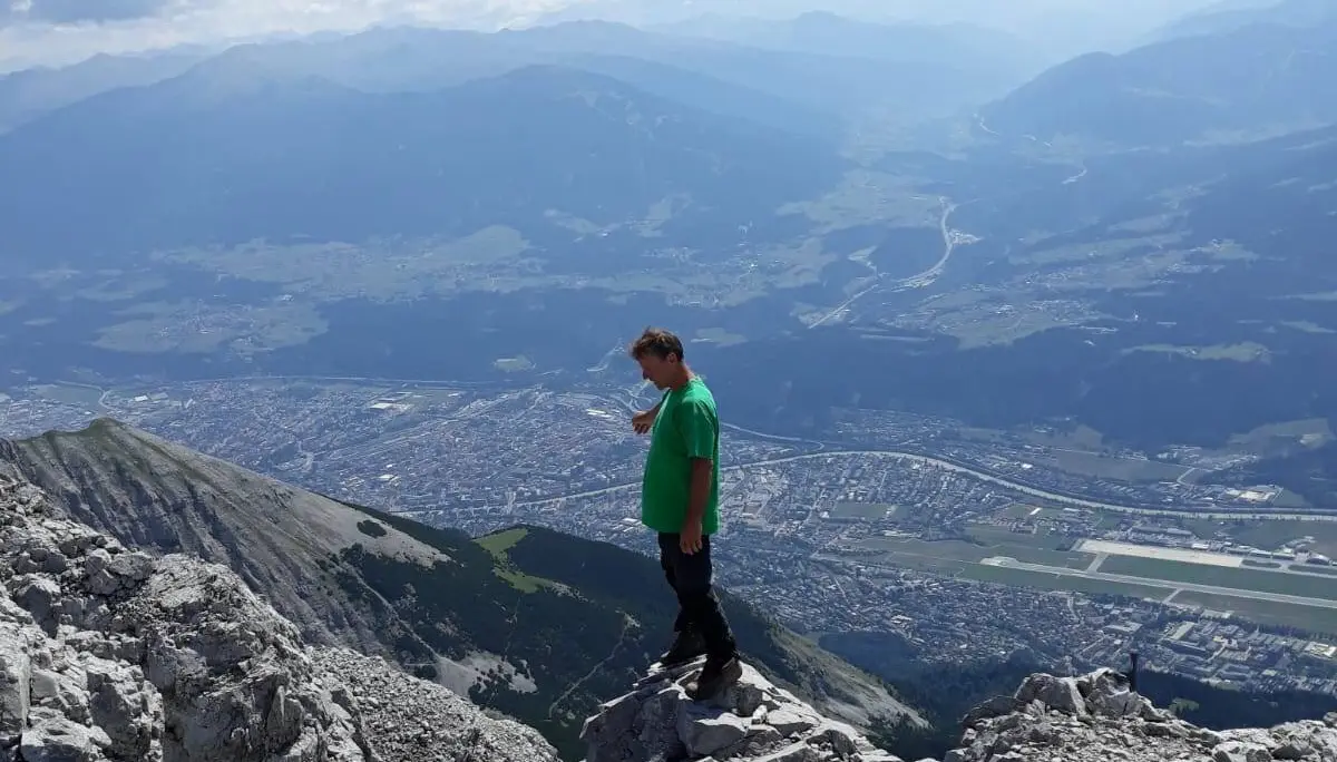 Ein Jugendlicher steht auf einem Felsvorsprung mit Blick auf das Tal und umliegende Berge. | © DAV Dortmund
