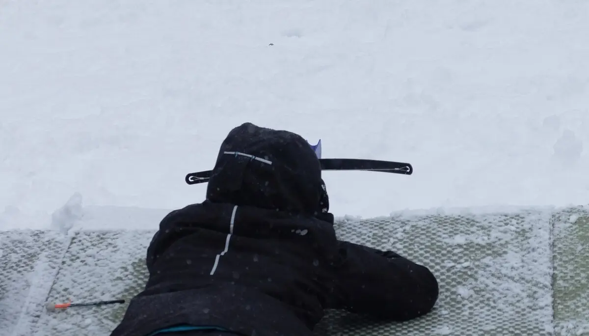 Kind liegt im Schnee und visiert eine Biathlon-Zielscheibe an, die aus runden Feldern besteht. | © DAV Dortmund