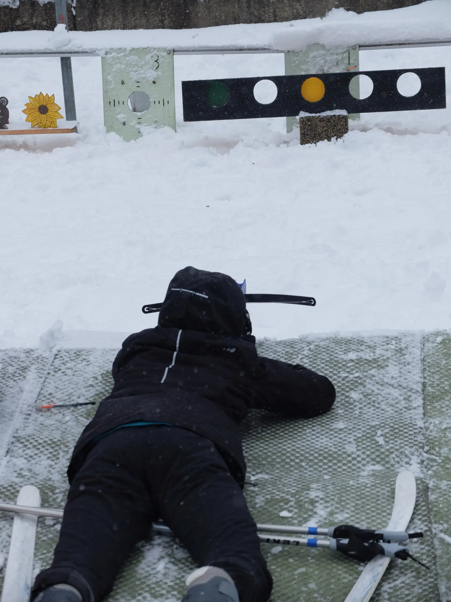 Kind liegt im Schnee und visiert eine Biathlon-Zielscheibe an, die aus runden Feldern besteht. | © DAV Dortmund