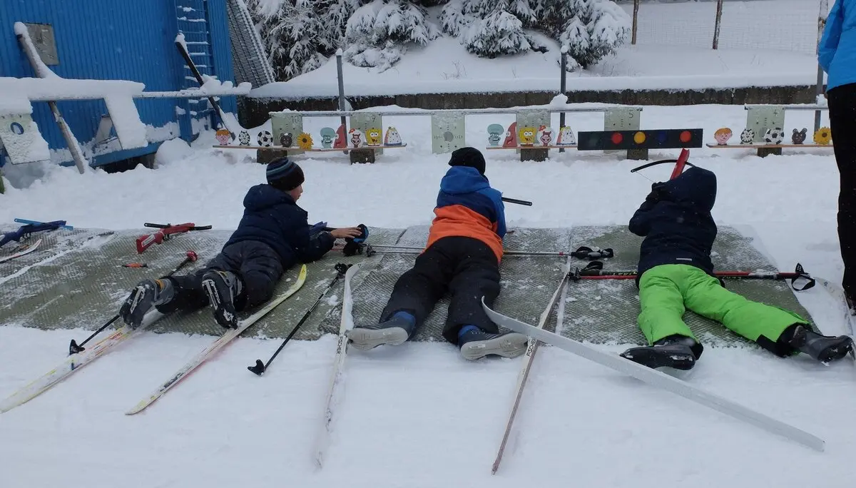 Drei Kinder liegen im Schnee auf Matten und zielen mit Biathlon-Gewehren auf Zielscheiben. | © DAV Dortmund