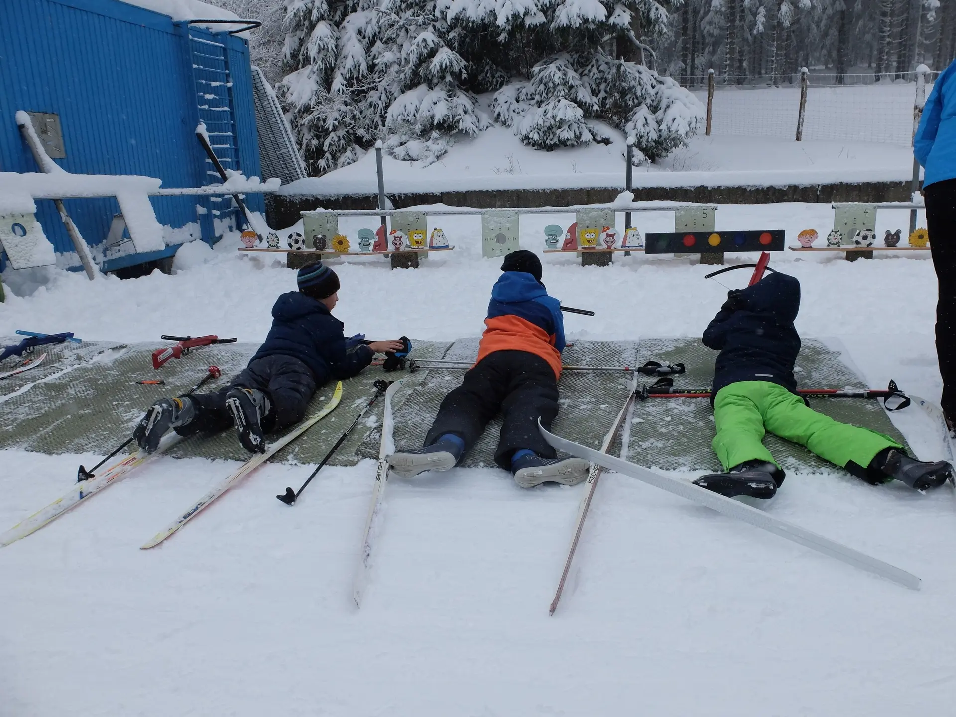 Drei Kinder liegen im Schnee auf Matten und zielen mit Biathlon-Gewehren auf Zielscheiben. | © DAV Dortmund