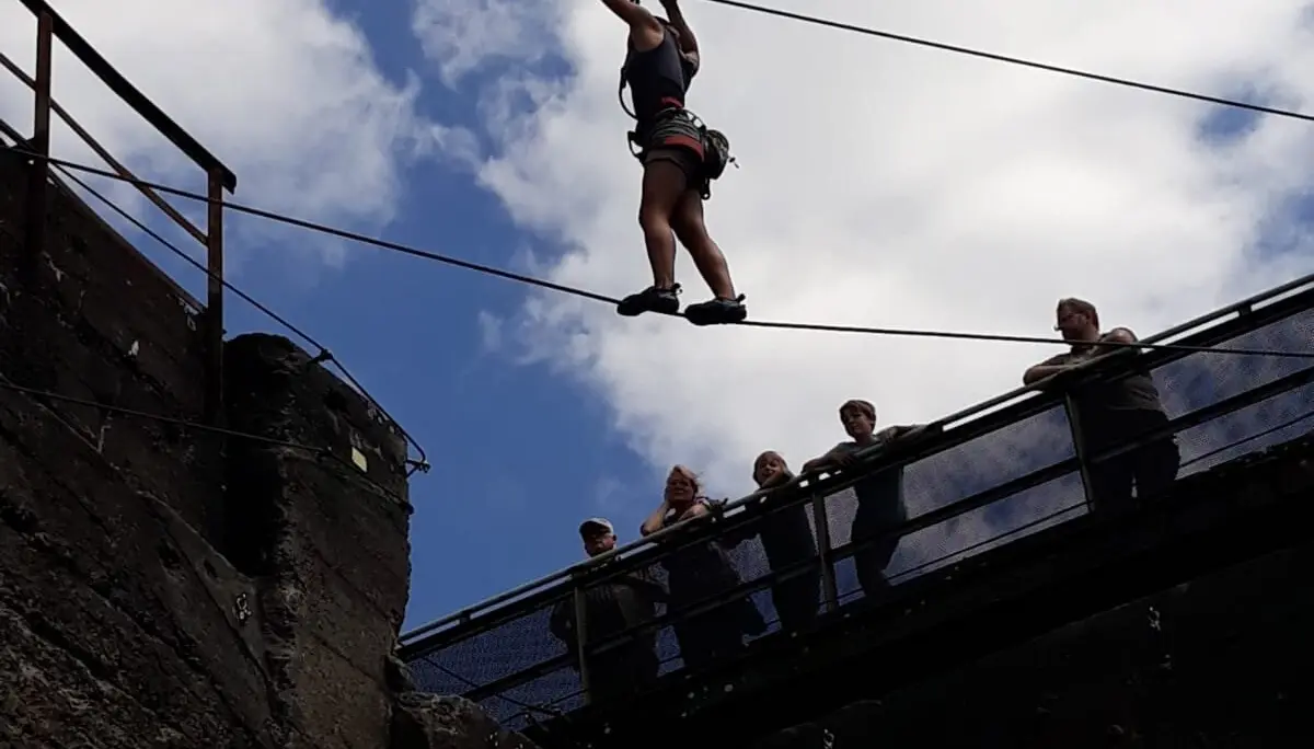 Eine Person balanciert an einem Seil zwischen zwei Betonwänden, mehrere Personen beobachten von oben. | © DAV Dortmund