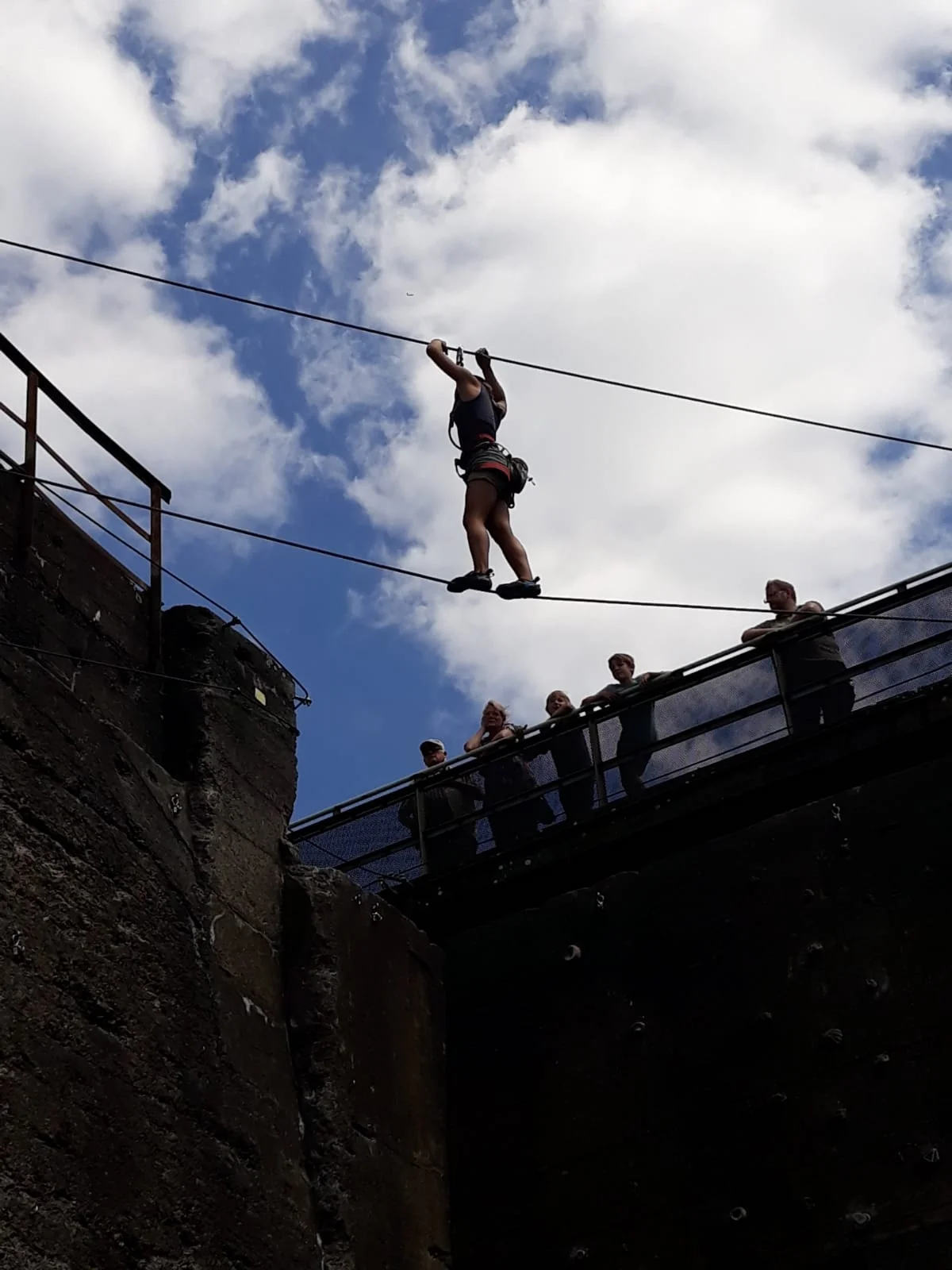 Eine Person balanciert an einem Seil zwischen zwei Betonwänden, mehrere Personen beobachten von oben. | © DAV Dortmund