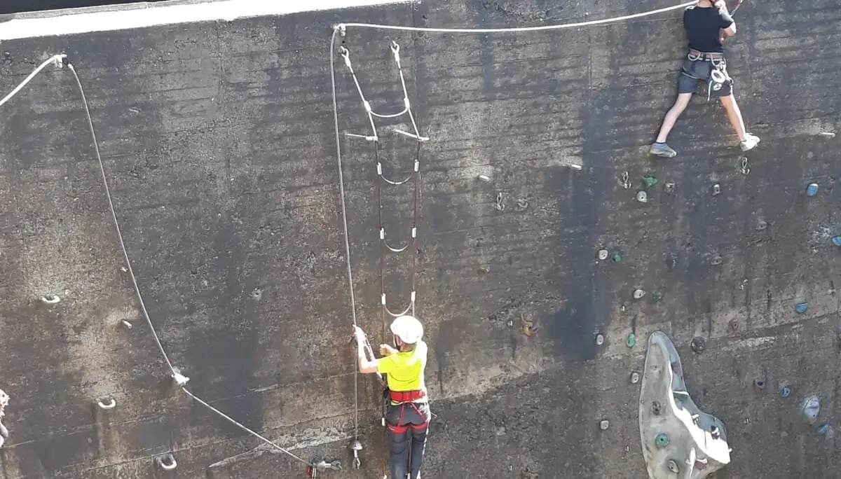 Drei Kinder klettern eine steile Betonwand mit künstlichen Griffen und Drahtseilen hinauf. | © DAV Dortmund