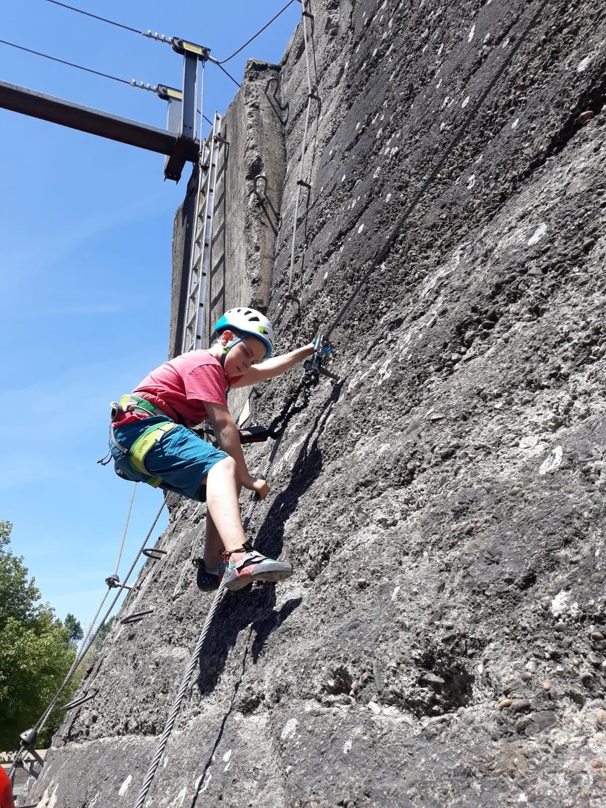 Ein Kind klettert gesichert an einer grauen Outdoor-Kletterwand bei Sonnenschein. | © DAV Dortmund