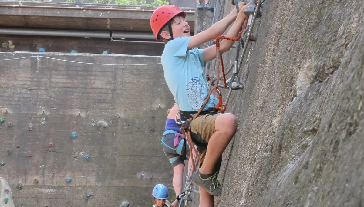 Jugendliche erklimmen eine Wand mit Eisenleitern im Klettersteig-Stil. | © DAV Dortmund