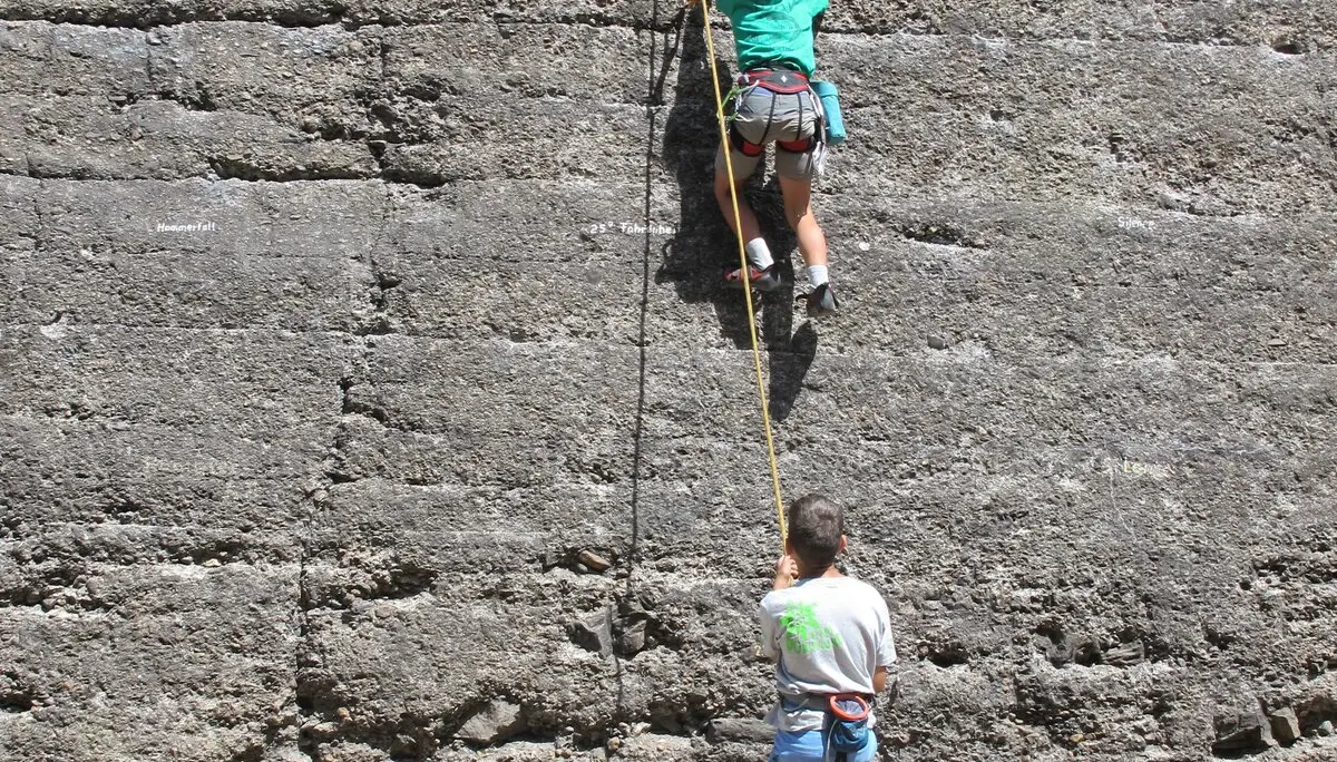 Ein Kind klettert an einer grauen Wand, eine Person sichert es von unten mit Seil. | © DAV Dortmund
