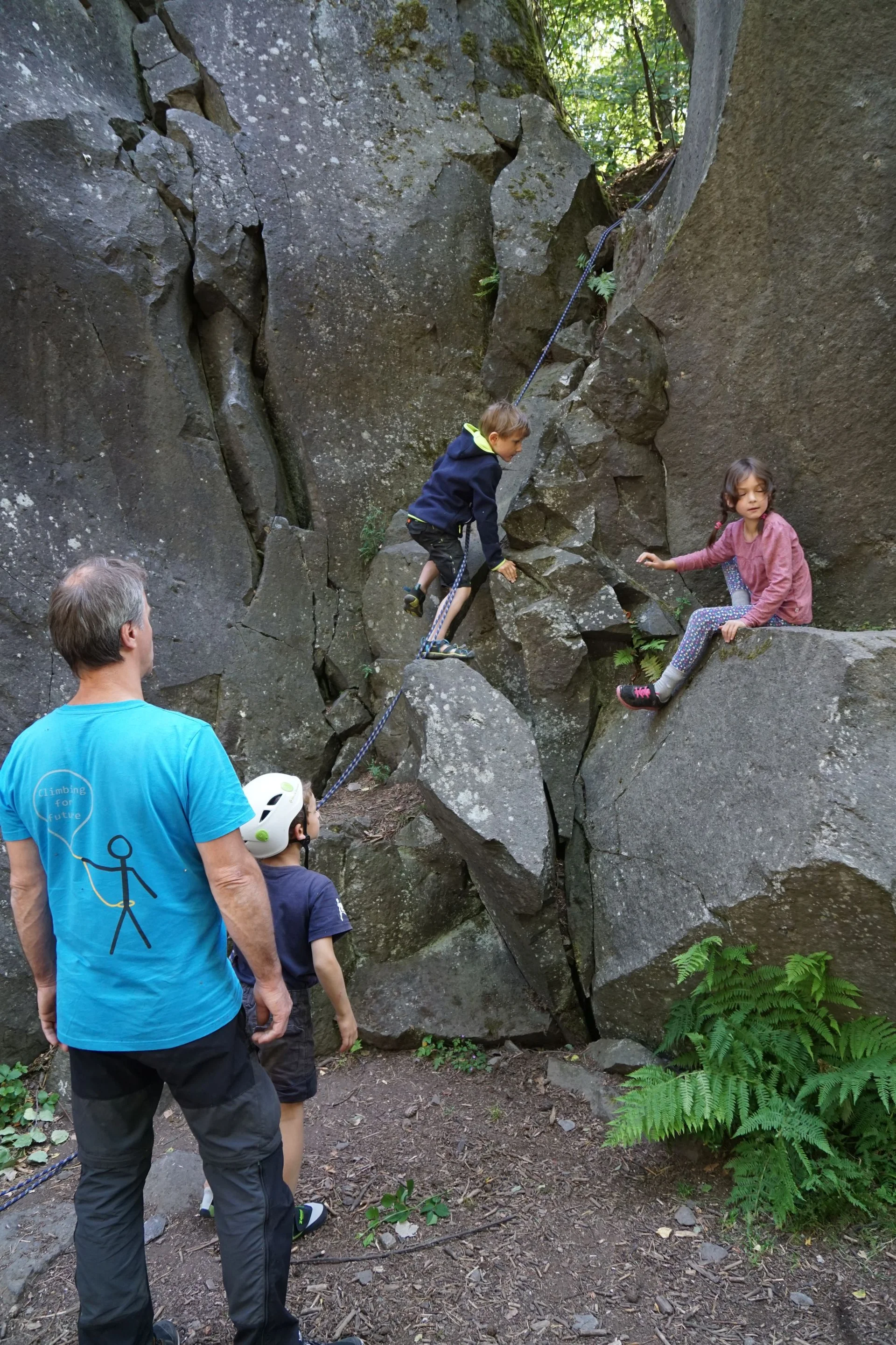 Zwei Kinder klettern zwischen Felsblöcken, ein Erwachsener sichert und beobachtet die Szene. | © DAV Dortmund
