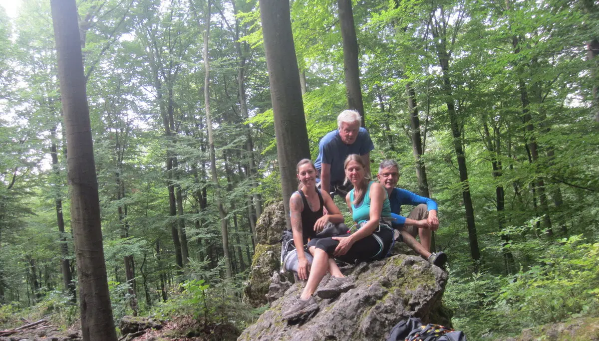 Vier Personen sitzen auf einem Felsen im Wald und lächeln in die Kamera, umgeben von Rucksäcken. | © DAV Dortmund