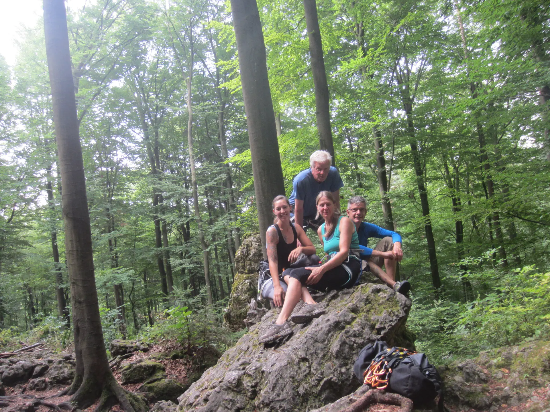 Vier Personen sitzen auf einem Felsen im Wald und lächeln in die Kamera, umgeben von Rucksäcken. | © DAV Dortmund