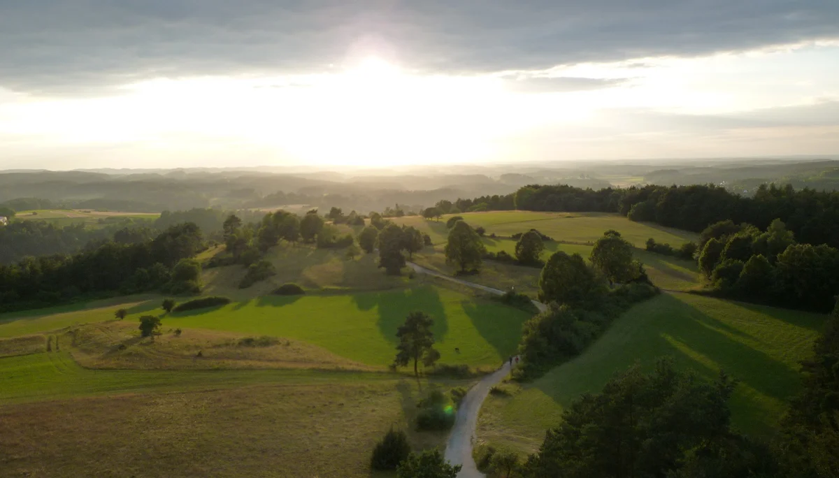 Sonnenuntergang über einer hügeligen Landschaft mit Feldern, Bäumen und einem geschwungenen Weg. | © DAV Dortmund