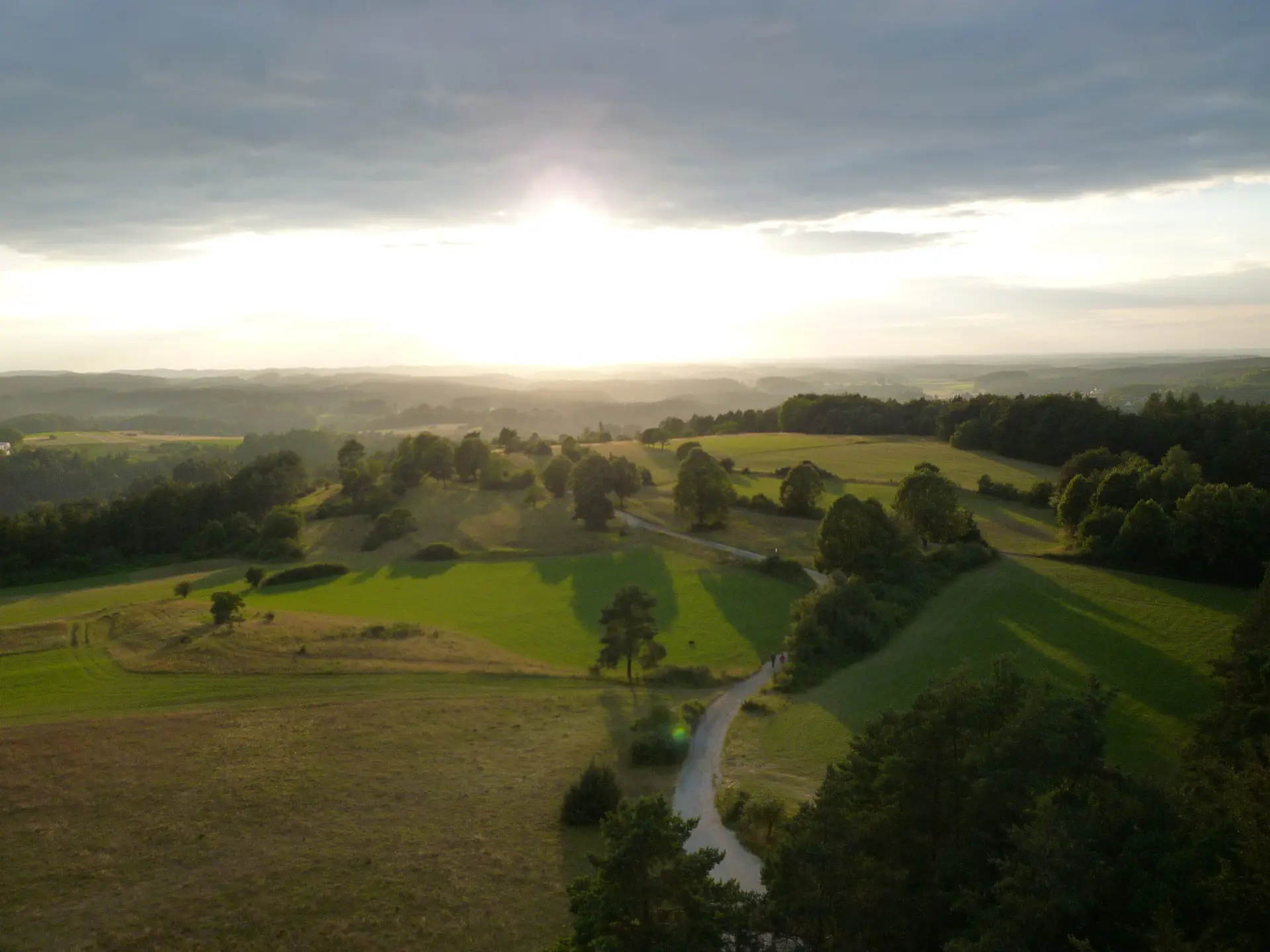 Sonnenuntergang über einer hügeligen Landschaft mit Feldern, Bäumen und einem geschwungenen Weg. | © DAV Dortmund