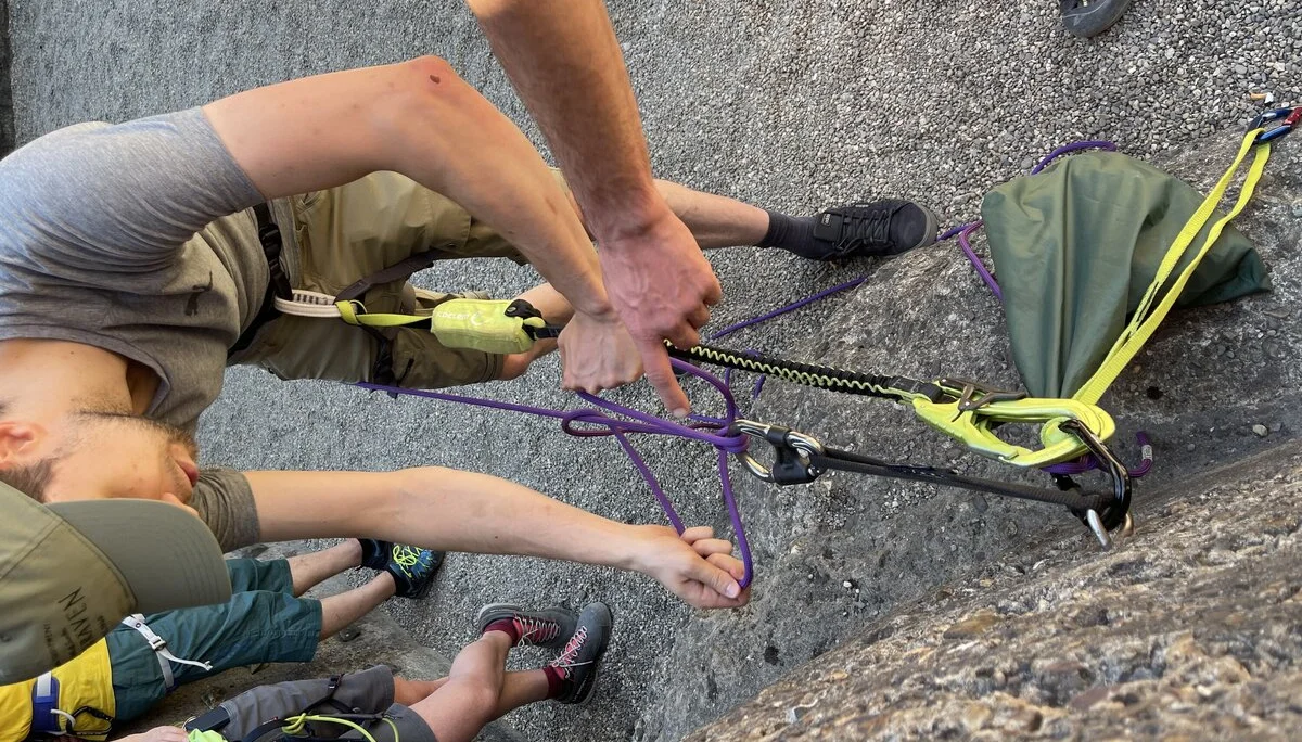 Ein junger Mann übt mit einem Partner den Aufbau eines Flaschenzugsystems am Fuß einer Wand. | © DAV Dortmund