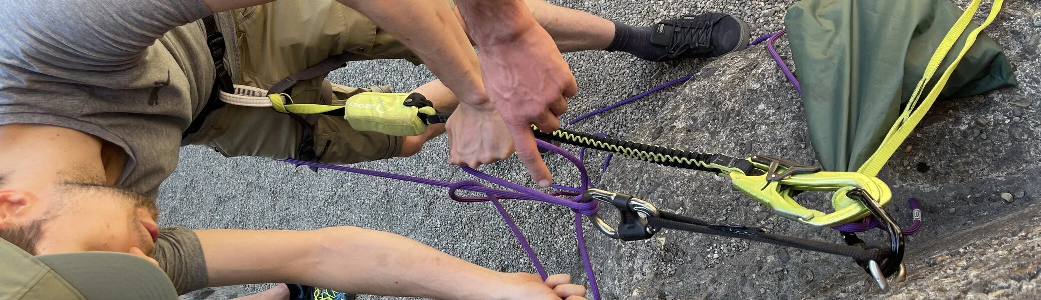 Ein junger Mann übt mit einem Partner den Aufbau eines Flaschenzugsystems am Fuß einer Wand. | © DAV Dortmund