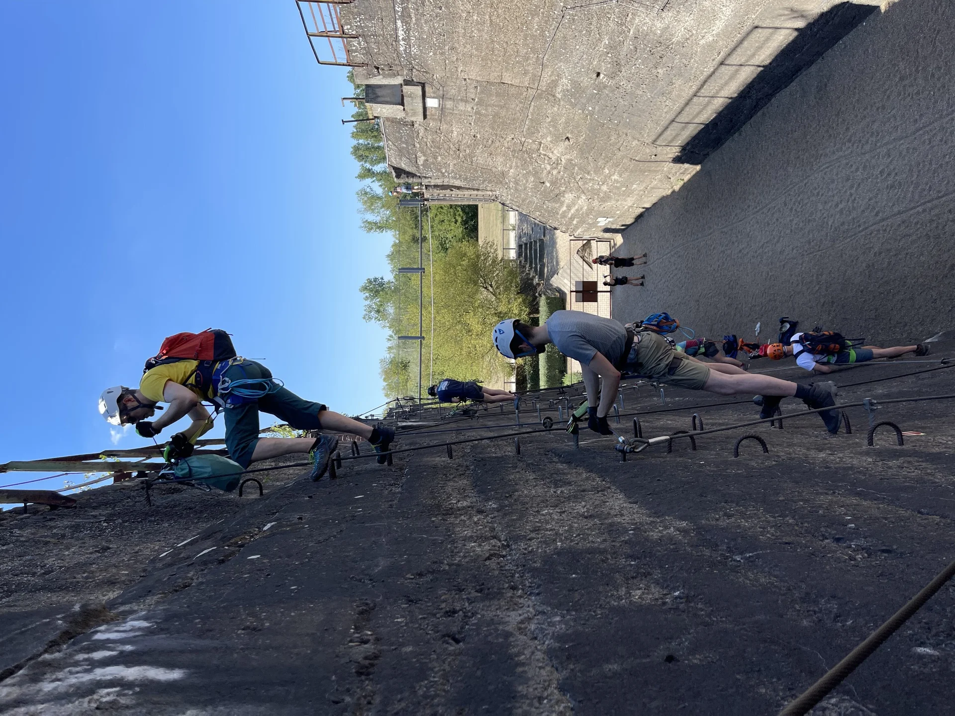 Teilnehmende steigen mit Kletterausrüstung einen künstlichen Klettersteig an einer hohen Betonwand empor. | © DAV Dortmund