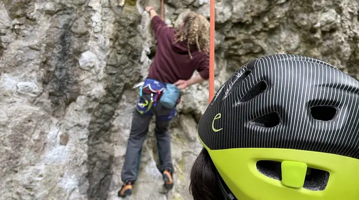 Eine Person mit Kletterhelm sichert eine andere, die eine steile Felswand hinaufklettert. | © DAV Dortmund