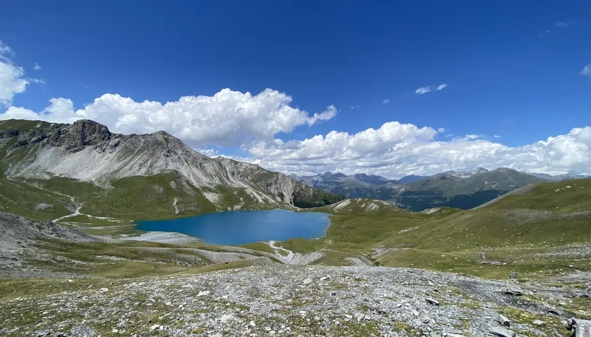 Ein klarer, blauer Bergsee liegt eingebettet in eine grüne Hügellandschaft unter blauem Himmel. | © DAV Dortmund