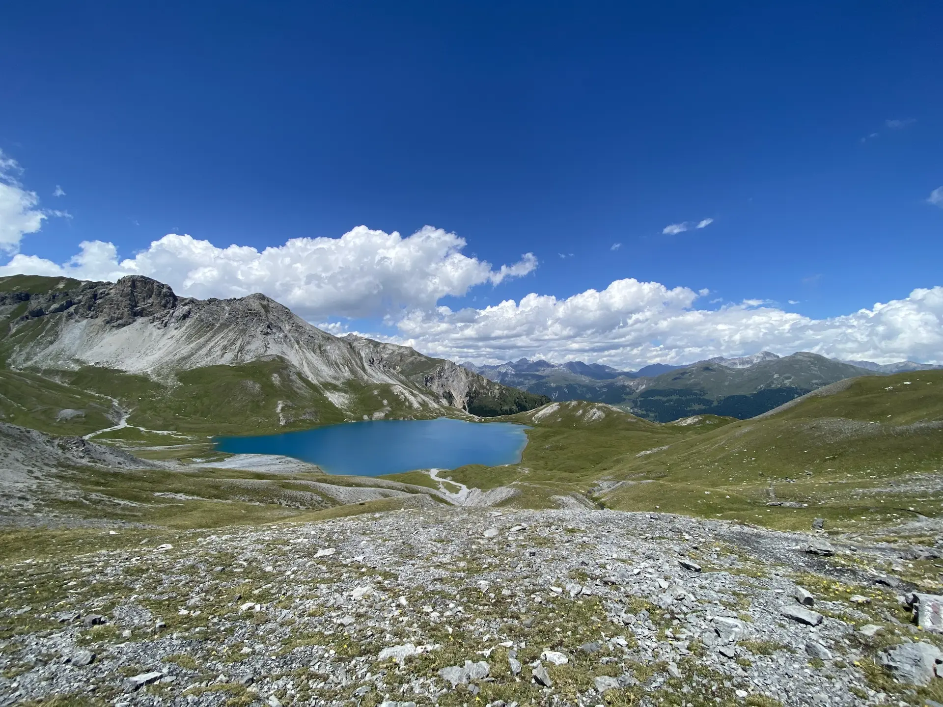 Ein klarer, blauer Bergsee liegt eingebettet in eine grüne Hügellandschaft unter blauem Himmel. | © DAV Dortmund