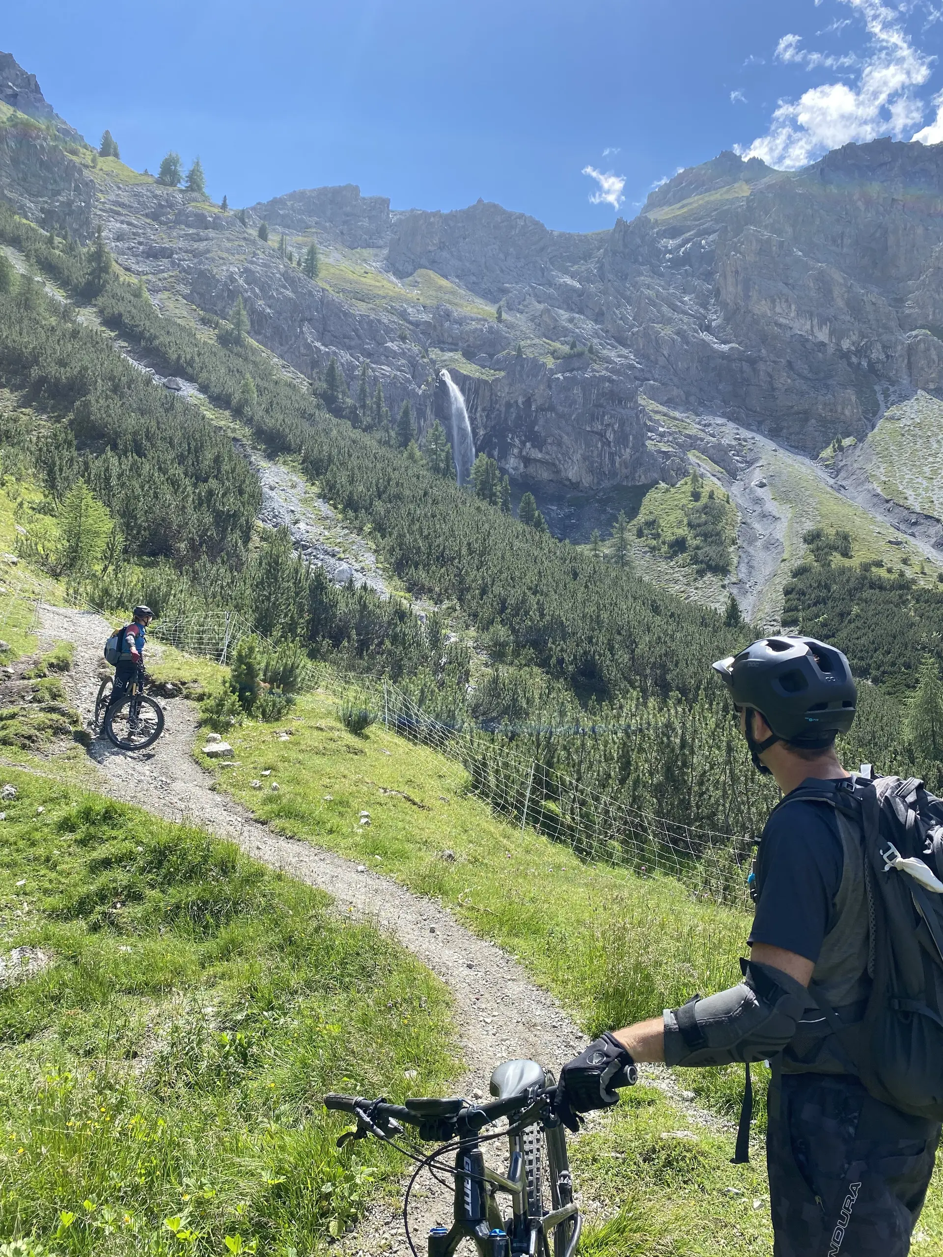 Zwei Mountainbiker auf einem grünen Wanderweg mit Wasserfall und steilen Berghängen im Hintergrund. | © DAV Dortmund
