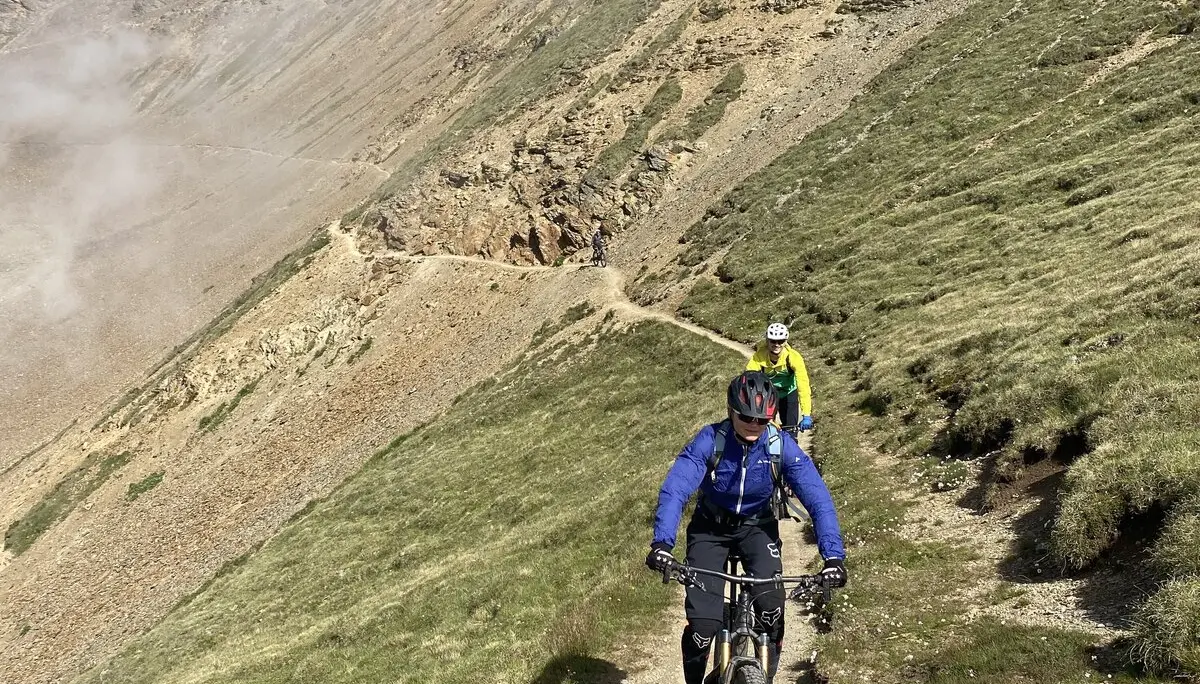 Zwei Mountainbiker fahren auf einem schmalen Pfad entlang eines Bergrückens bei Sonne und Nebel. | © DAV Dortmund