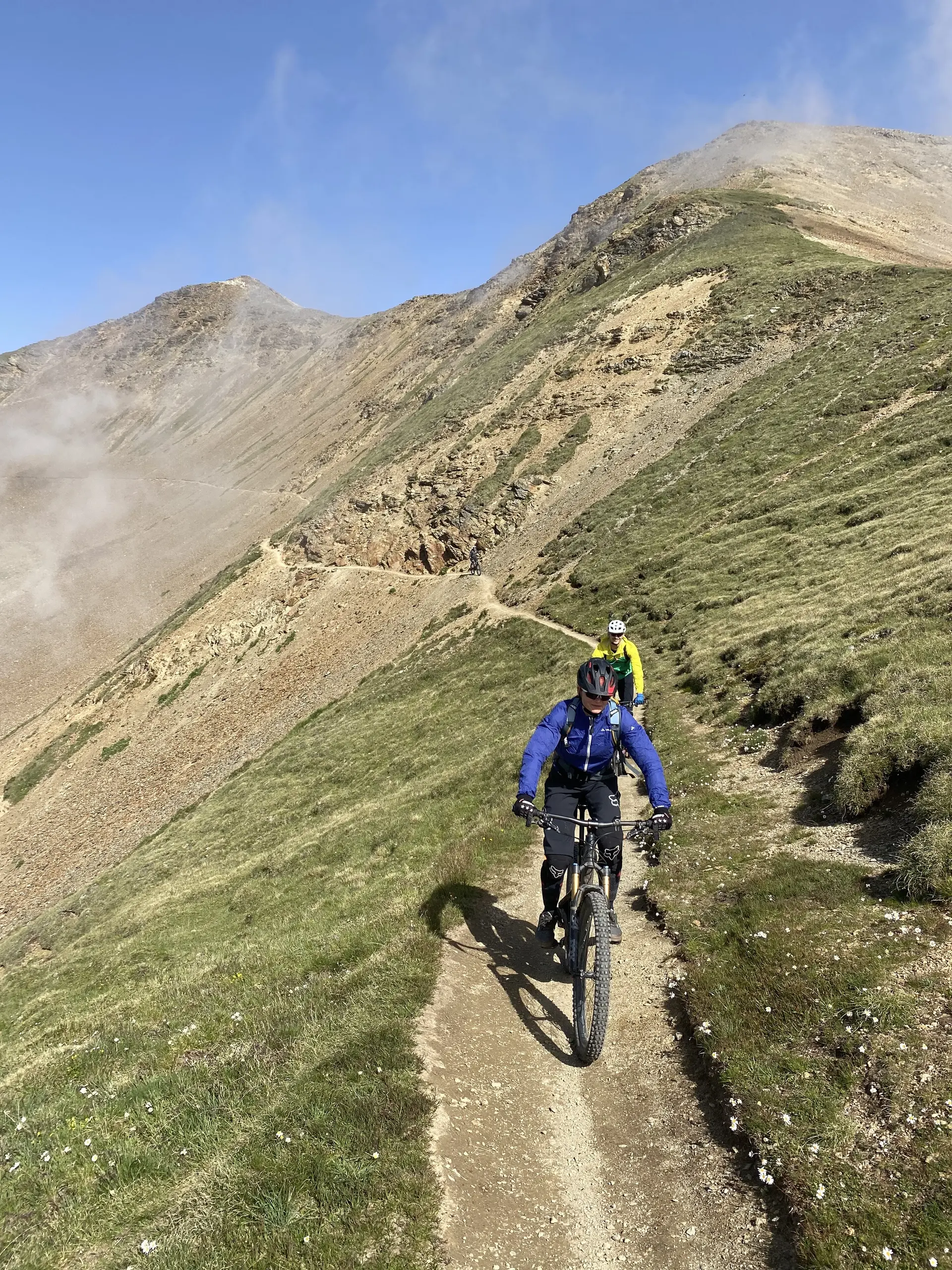 Zwei Mountainbiker fahren auf einem schmalen Pfad entlang eines Bergrückens bei Sonne und Nebel. | © DAV Dortmund