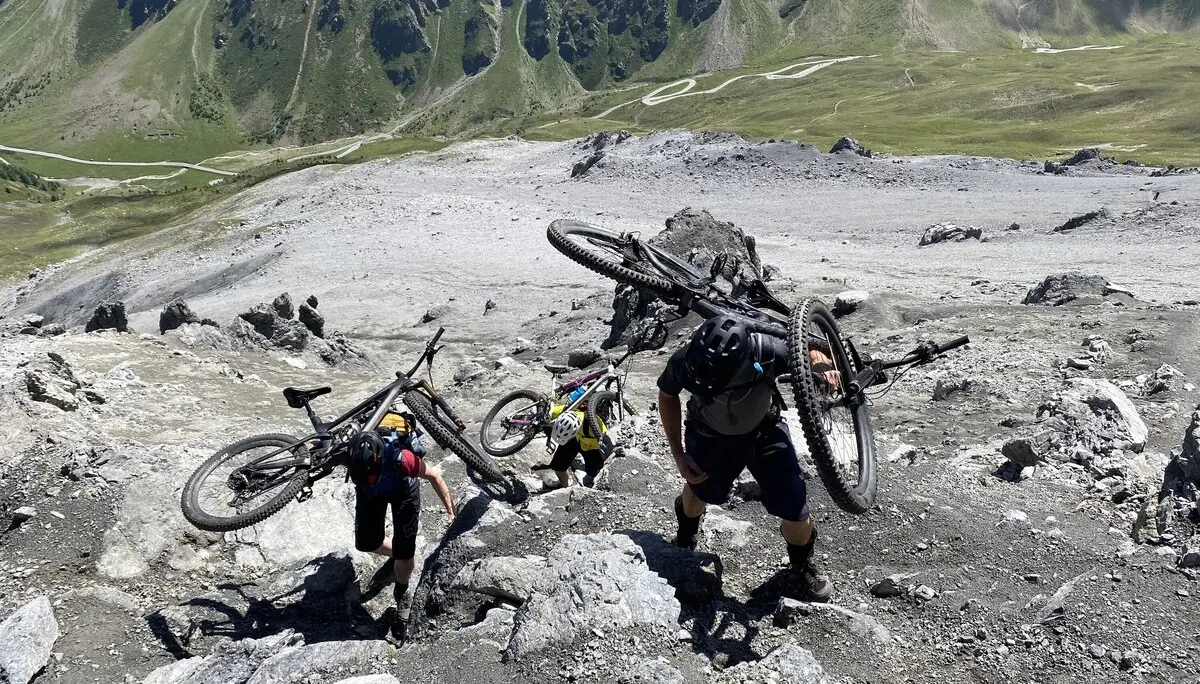 Drei Personen tragen ihre Mountainbikes über ein steiles, felsiges Gelände im Hochgebirge. | © DAV Dortmund