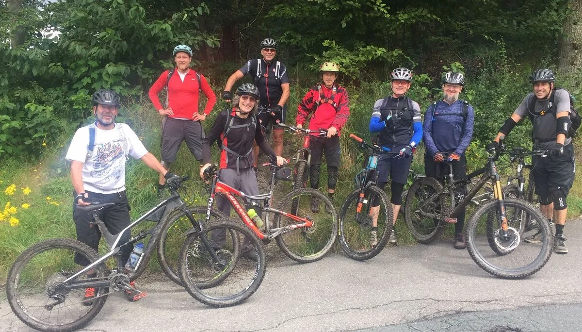 Acht Personen mit Helmen und Bikes stehen auf einer Straße am Waldrand und lächeln in die Kamera. | © DAV Dortmund