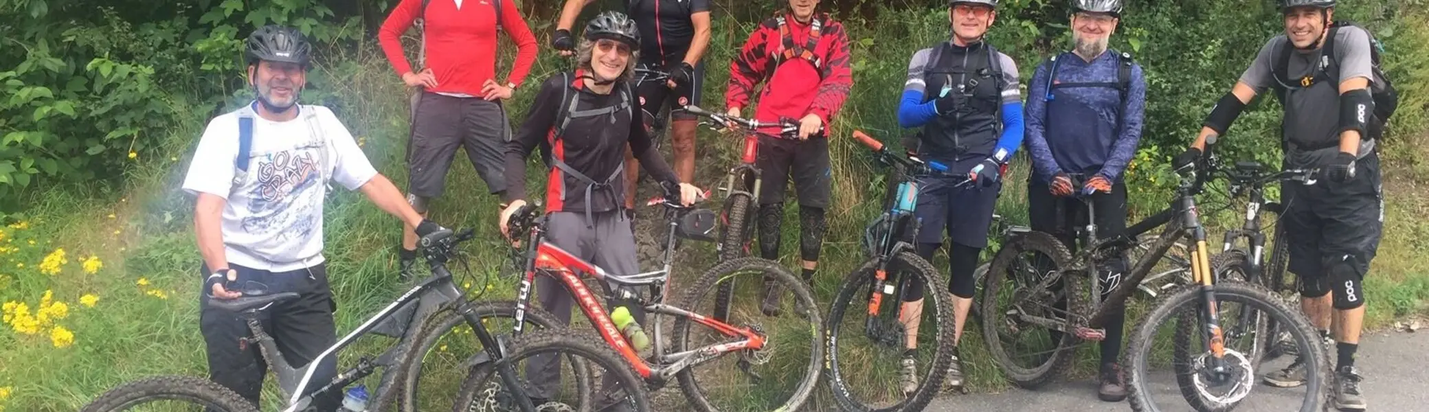 Acht Personen mit Helmen und Bikes stehen auf einer Straße am Waldrand und lächeln in die Kamera. | © DAV Dortmund
