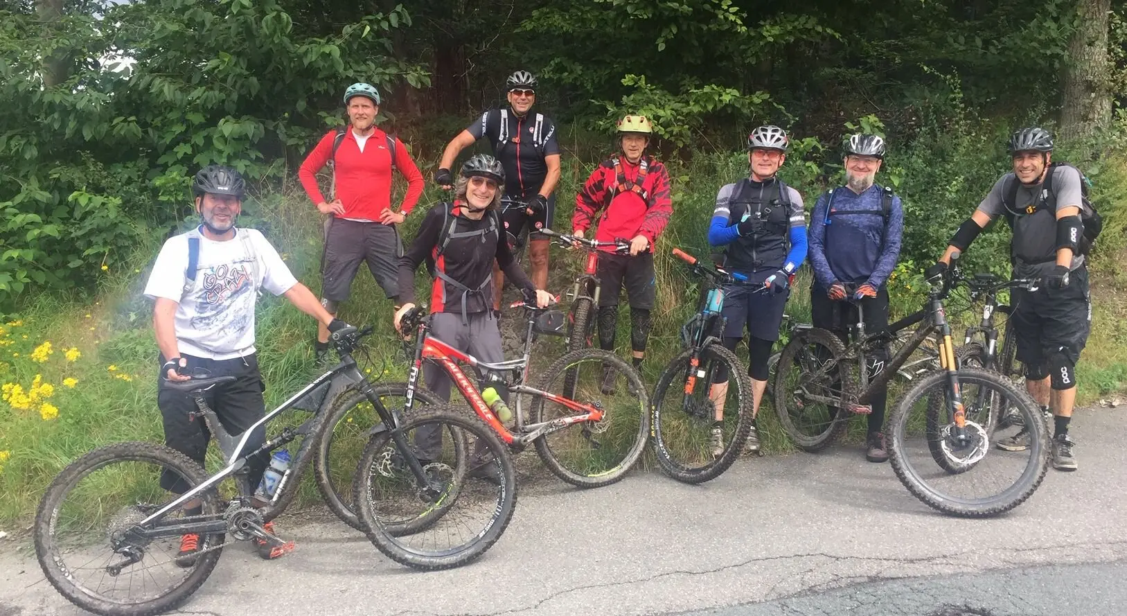 Acht Personen mit Helmen und Bikes stehen auf einer Straße am Waldrand und lächeln in die Kamera. | © DAV Dortmund