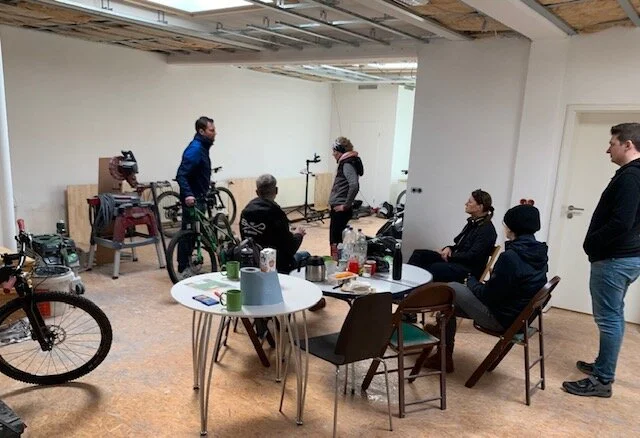 Mehrere Personen sitzen und stehen in einer Fahrradwerkstatt mit Werkzeugen und Rädern. | © DAV Dortmund
