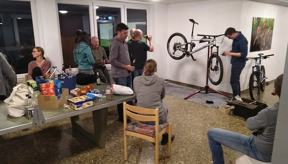Mehrere Personen sitzen und stehen in einem Raum mit Werkzeugen, während zwei Mountainbikes gewartet werden. | © DAV Dortmund