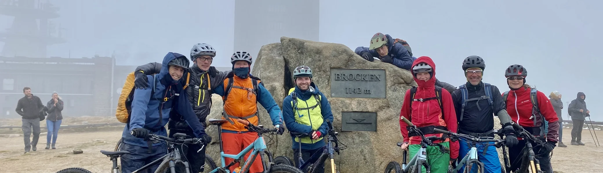 Acht Radfahrende stehen mit ihren Mountainbikes vor dem Brockenstein im Nebel. | © DAV Dortmund