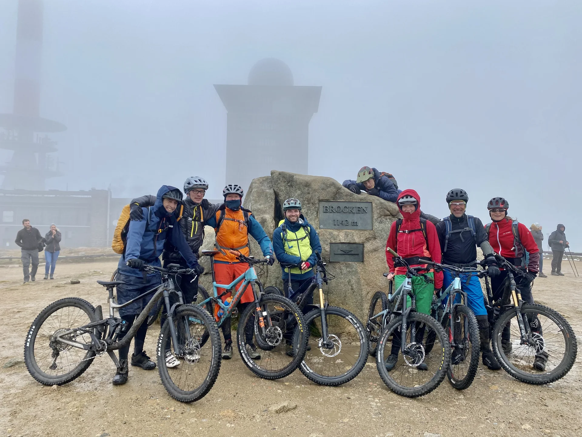 Acht Radfahrende stehen mit ihren Mountainbikes vor dem Brockenstein im Nebel. | © DAV Dortmund