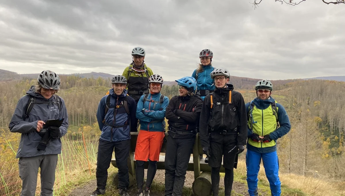 Acht Personen mit Helmen posieren an einem Aussichtspunkt mit weitem Blick über den herbstlichen Wald. | © DAV Dortmund