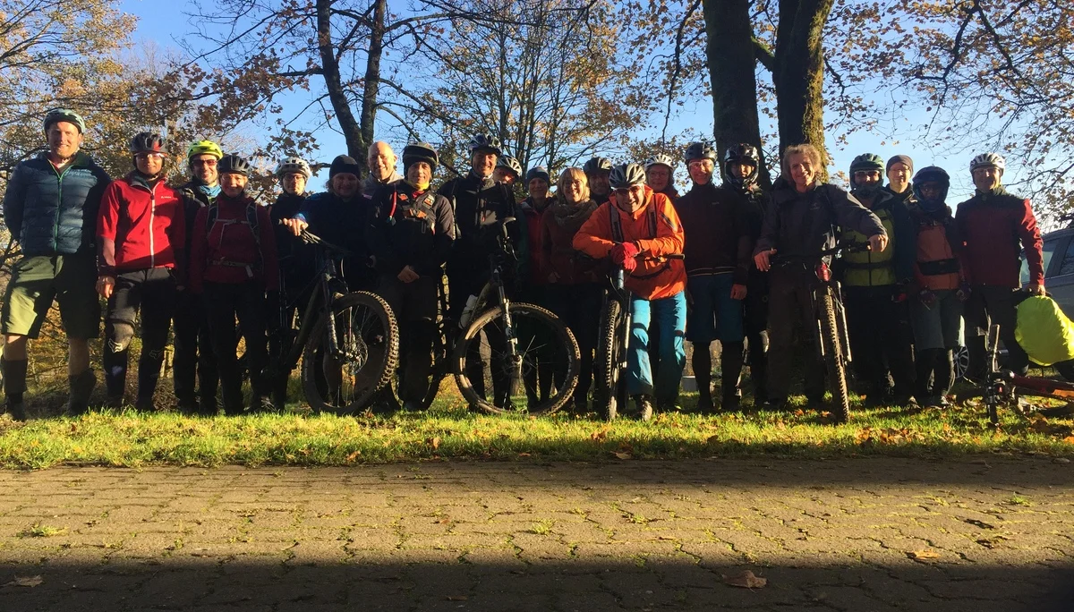 Eine große Gruppe von Mountainbiker*innen mit Fahrrädern steht im Schatten unter Bäumen bei tiefstehender Sonne. | © DAV Dortmund