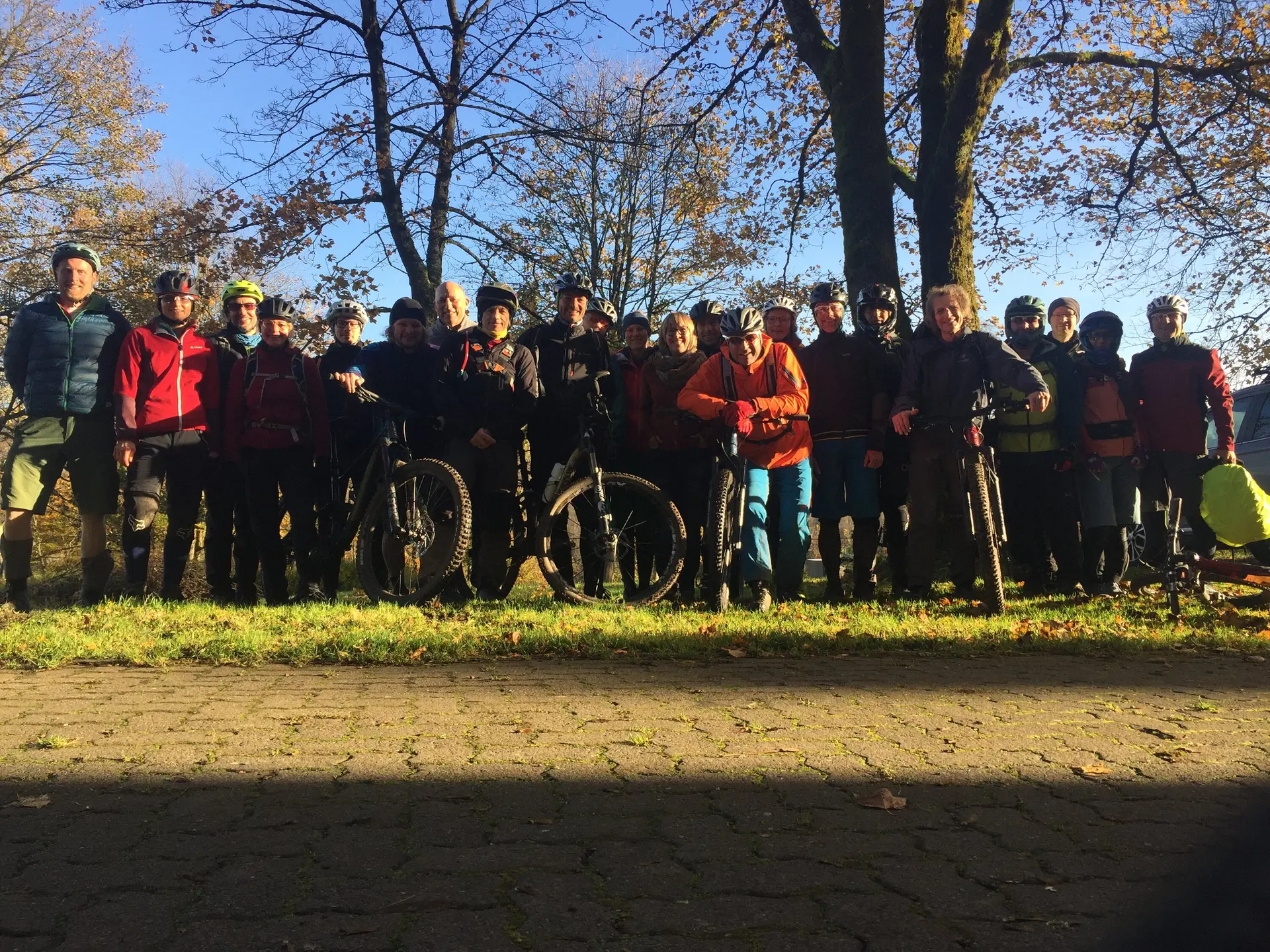 Eine große Gruppe von Mountainbiker*innen mit Fahrrädern steht im Schatten unter Bäumen bei tiefstehender Sonne. | © DAV Dortmund