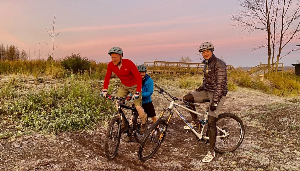 Drei Personen auf zwei Mountainbikes fahren bei frostigem Wetter durch eine flache Landschaft im Morgengrauen. | © DAV Dortmund