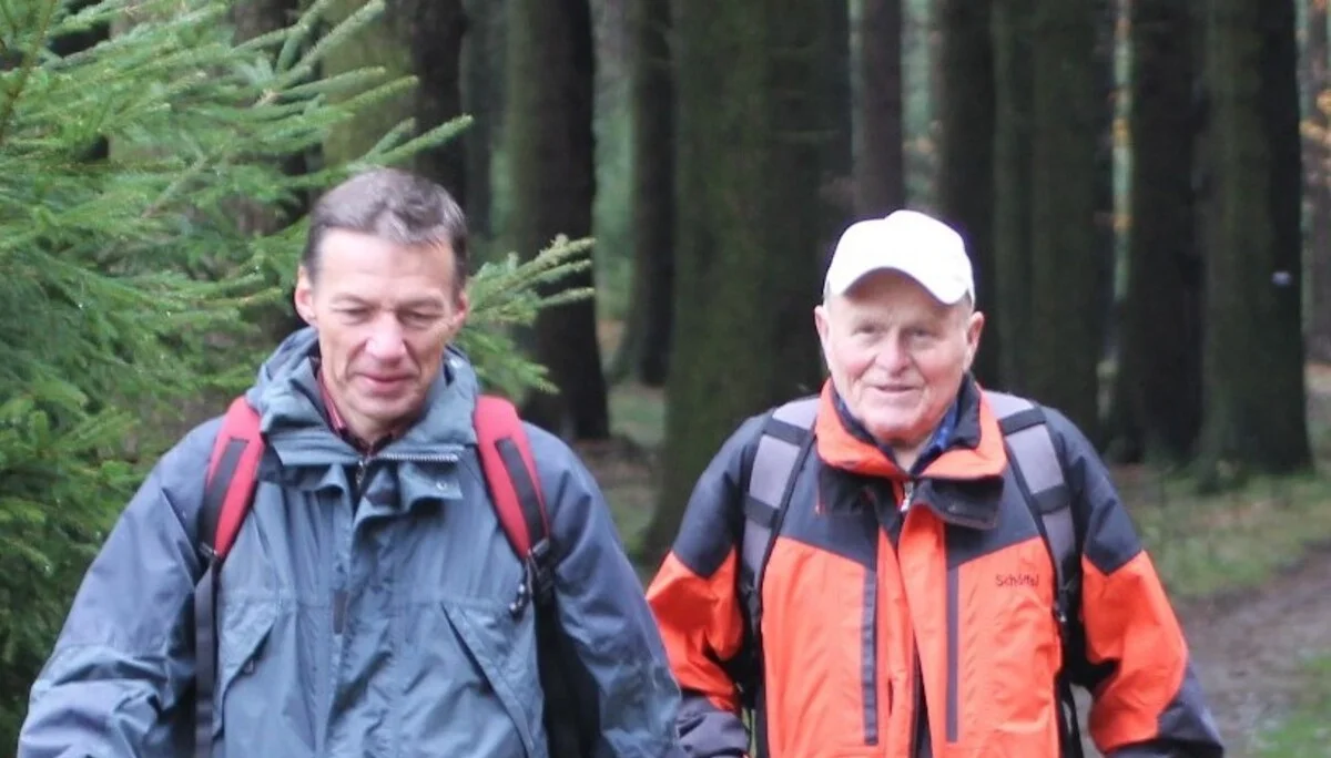 Zwei Männer in wetterfester Kleidung wandern gemeinsam auf einem Waldweg. | © DAV Dortmund
