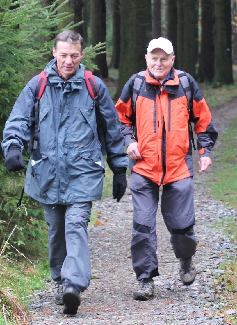 Zwei Männer in wetterfester Kleidung wandern gemeinsam auf einem Waldweg. | © DAV Dortmund