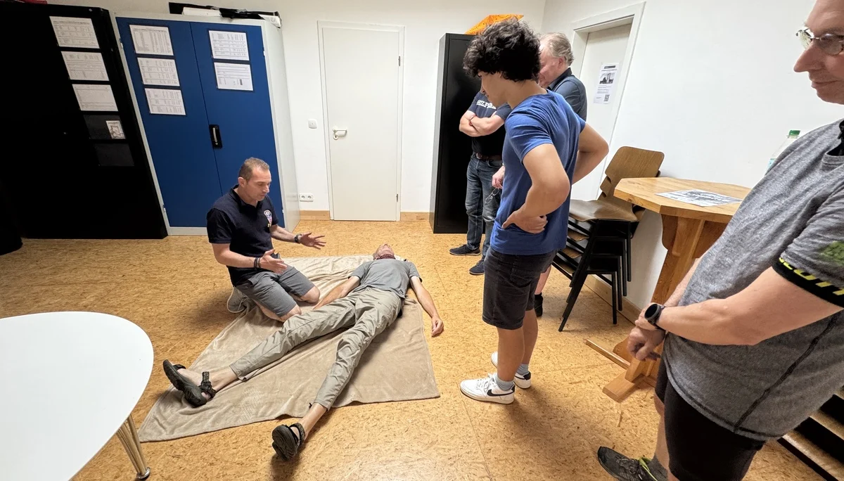 Ein Teilnehmer demonstriert die stabile Seitenlage an einer Person auf einer Decke, andere beobachten. | © DAV Dortmund