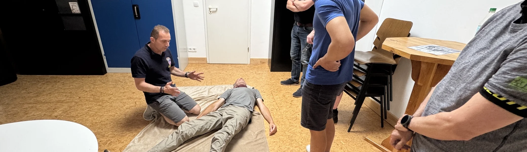 Ein Teilnehmer demonstriert die stabile Seitenlage an einer Person auf einer Decke, andere beobachten. | © DAV Dortmund