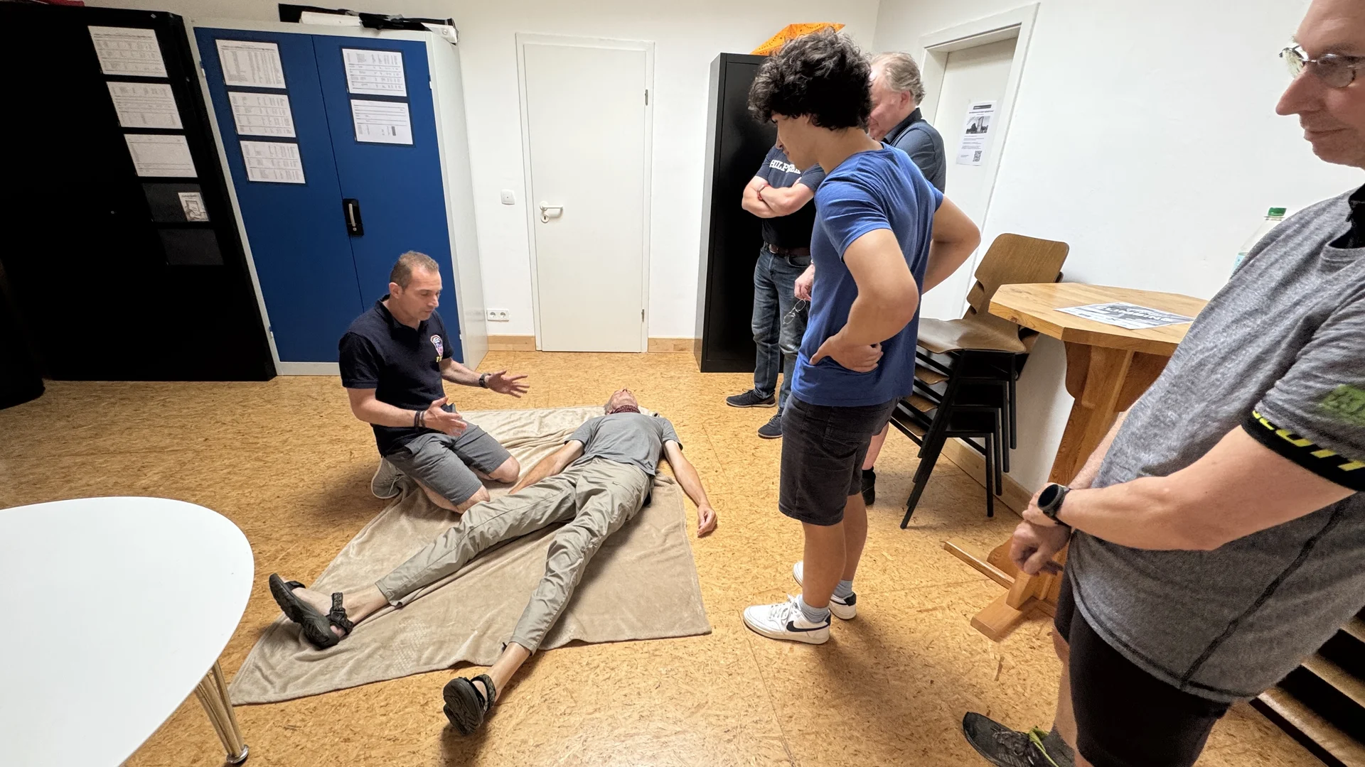 Ein Teilnehmer demonstriert die stabile Seitenlage an einer Person auf einer Decke, andere beobachten. | © DAV Dortmund