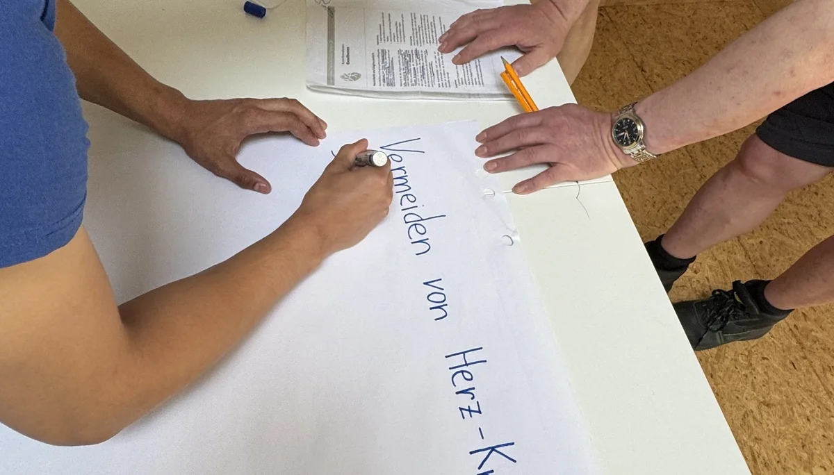 Ein junger Mann schreibt auf ein großes Blatt Papier, während andere Personen zusehen. | © DAV Dortmund