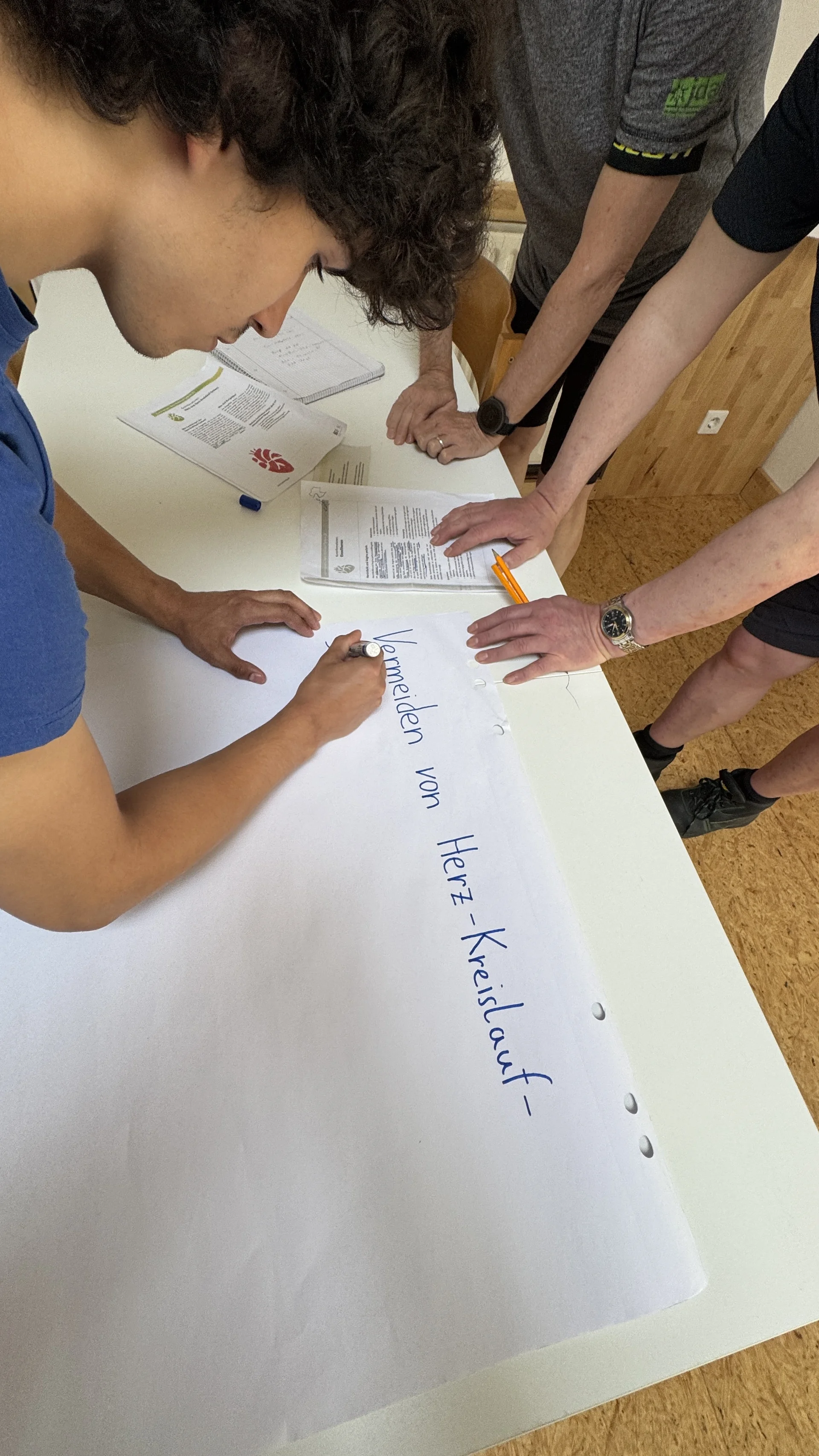 Ein junger Mann schreibt auf ein großes Blatt Papier, während andere Personen zusehen. | © DAV Dortmund